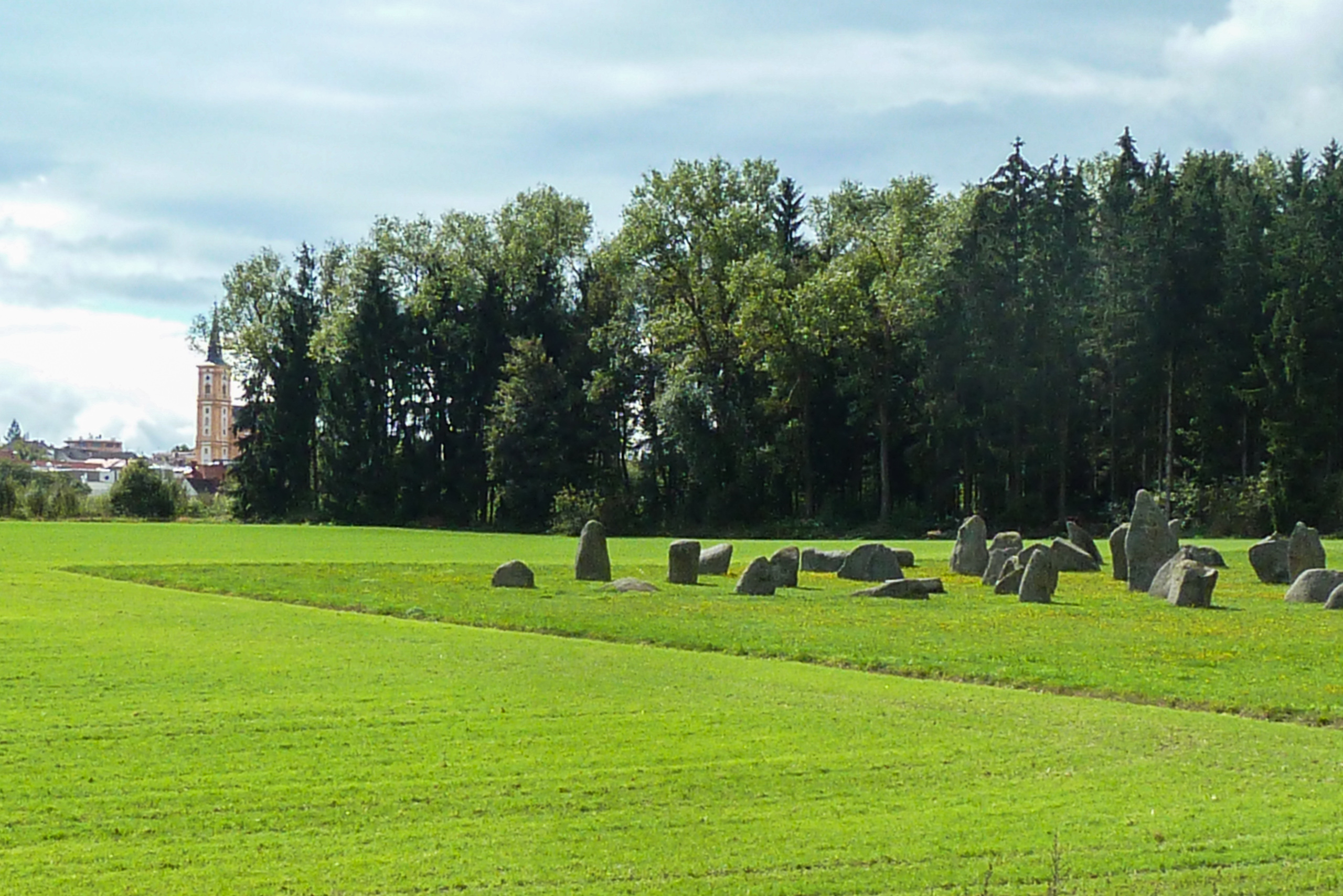 Steinkreis auf einer Wiese, dahinter ein Kirchturm